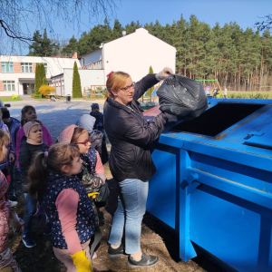 Uczniowie klasy 1 wspólnie wyrzucają do pojemnika zebrane śmieci